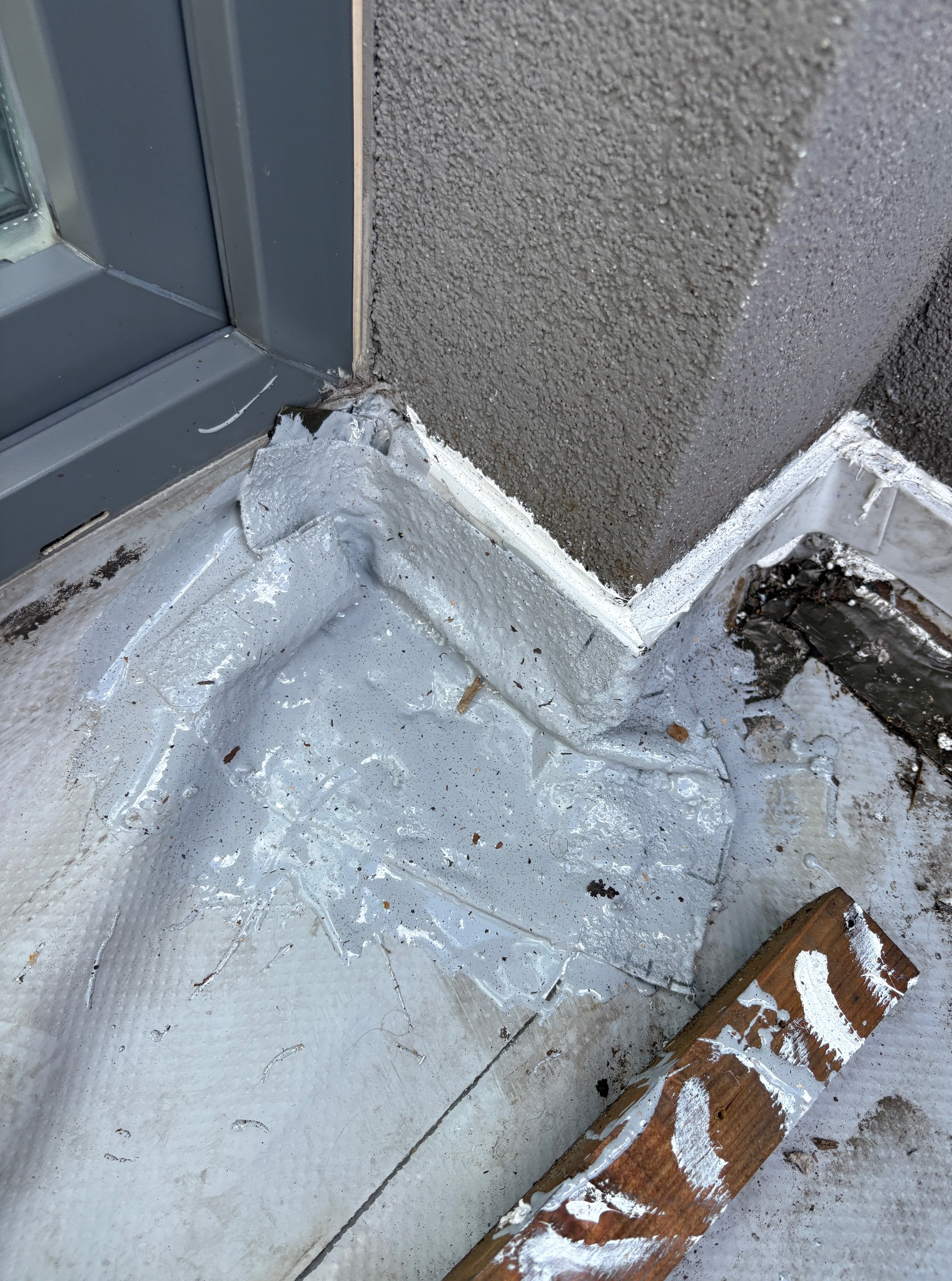 Szczegółowe ujęcie izolacji przeciwwodnej, na styku okna i ściany zewnętrznej, z widocznymi śladami farby na drewnianej desce obok.