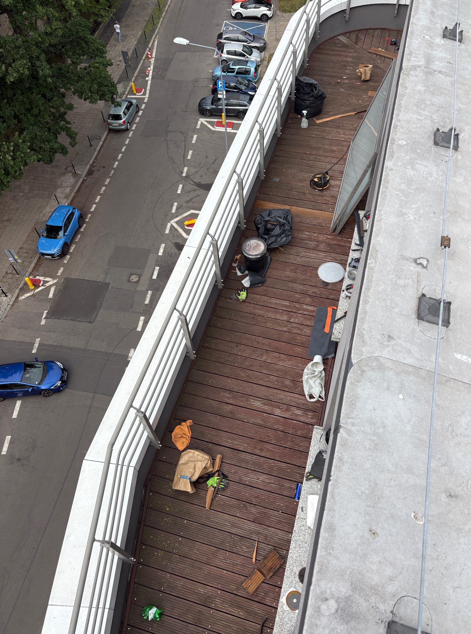 Widok z góry na taras z drewnianą podłogą i białymi balustradami, na którym znajdują się narzędzia i materiały budowlane, sugerujące trwające prace wykończeniowe.