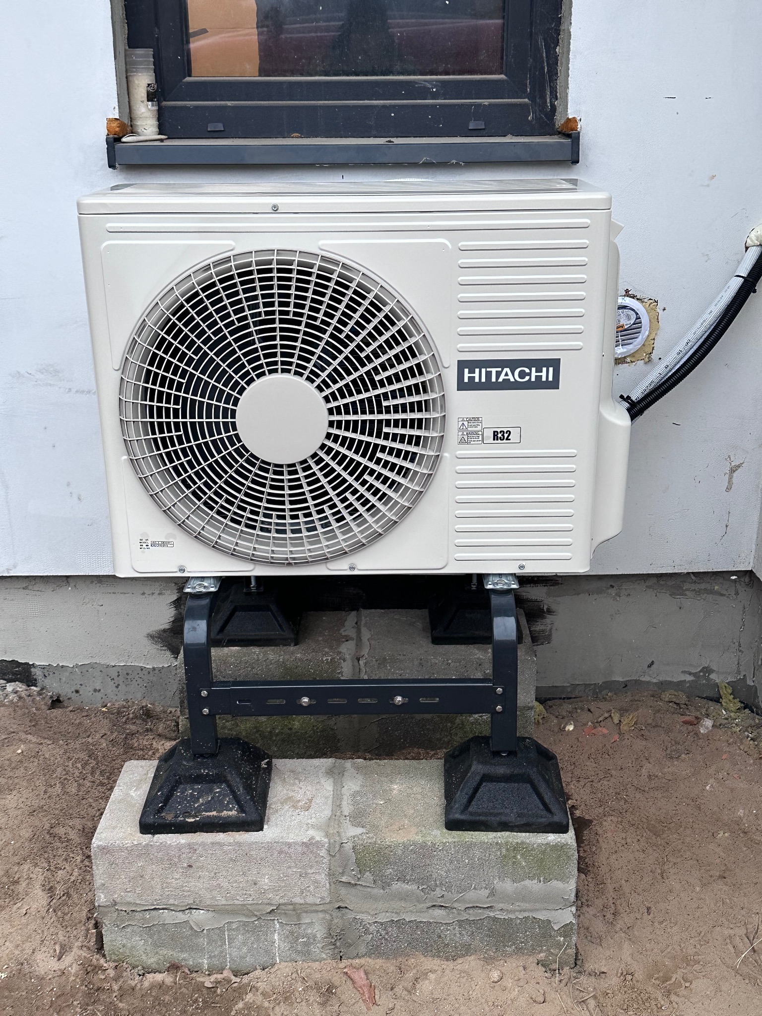 Klimatyzator Hitachi, model R32, zamontowany na zewnątrz budynku w Ostrowi Mazowieckiej, widoczny przewód instalacyjny i podstawa montażowa.
