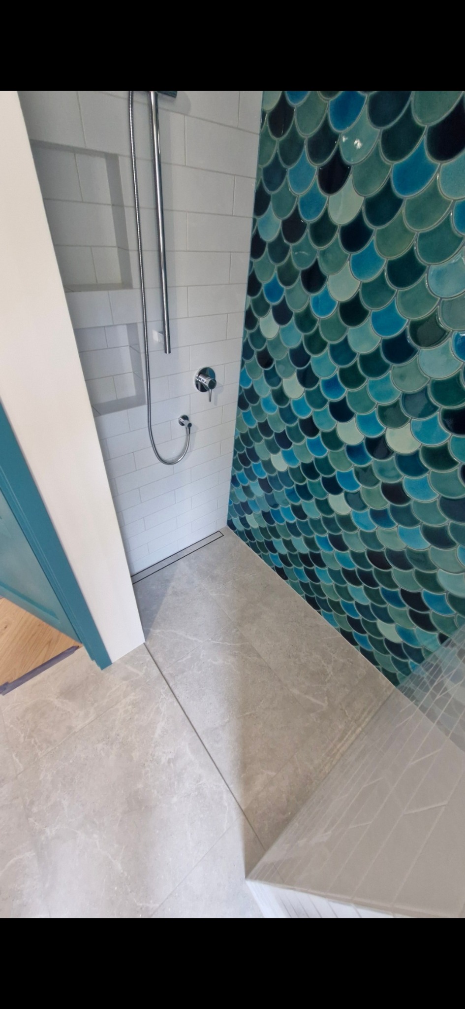 Wykończona kabina prysznicowa z białą i turkusową glazurą w kształcie rybiej łuski oraz szarą podłogą z marmuru. Nowoczesny design.
