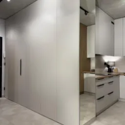 Nowoczesna kuchnia z zabudową meblową w odcieniach szarości, z lustrzaną ścianą. Widoczny fragment blatu i szafek. Minimalistyczny design, surowy beton na suficie.