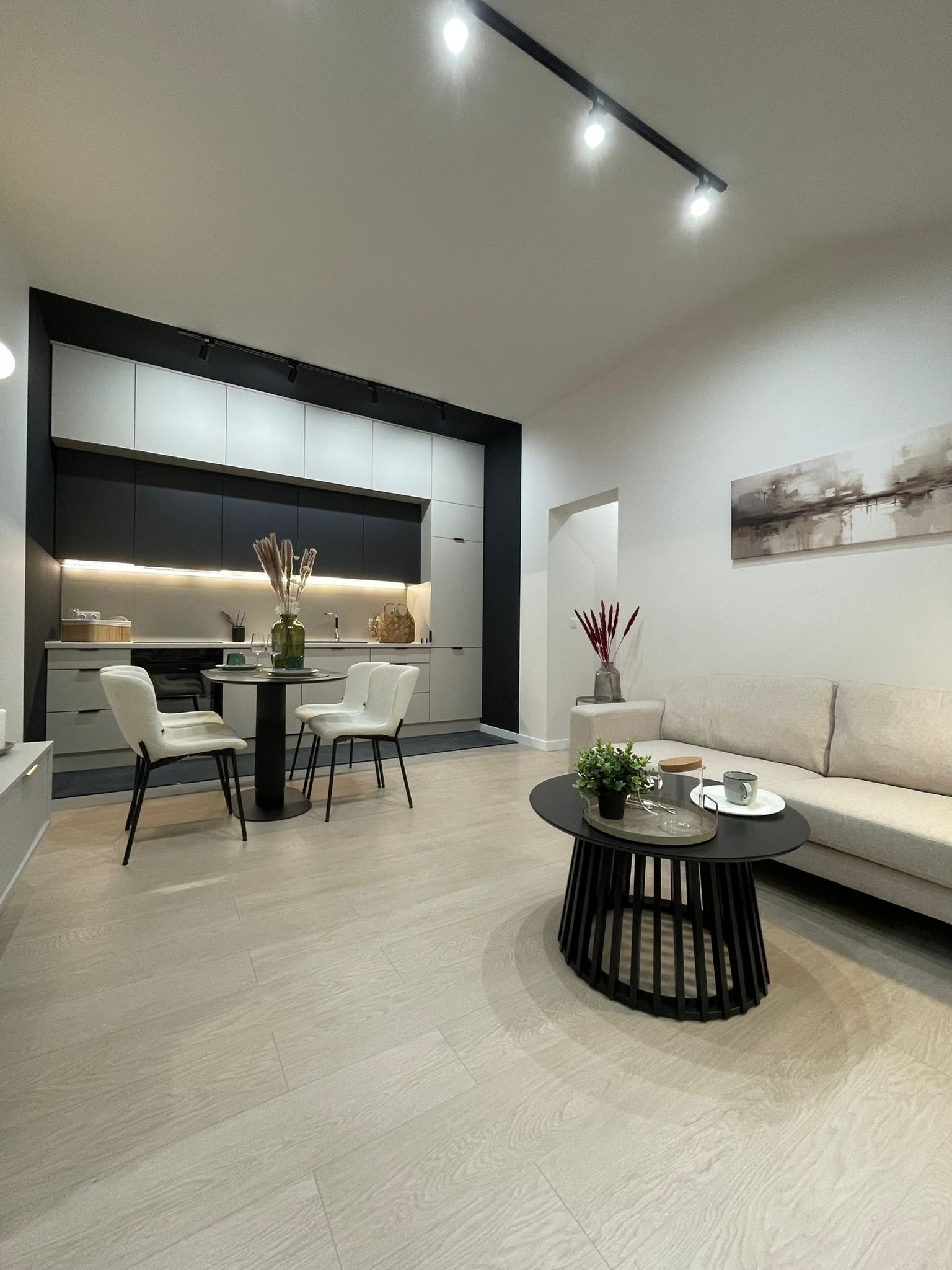 Jasne wnętrze po remoncie w Katowicach: minimalistyczna kuchnia z czarnymi akcentami, okrągły stół z krzesłami i sofa z obrazem na ścianie. Nowoczesny design.