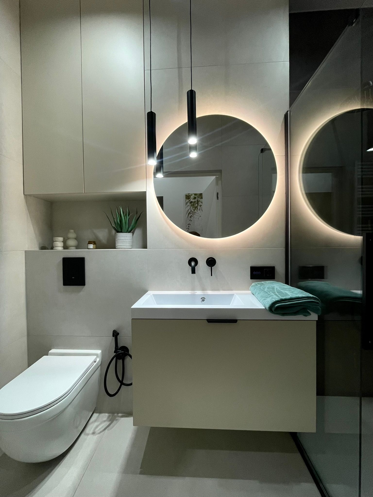 Nowoczesna łazienka po remoncie: podwieszana toaleta, szafka z umywalką, okrągłe lustro z podświetleniem LED i minimalistyczne lampy wiszące.