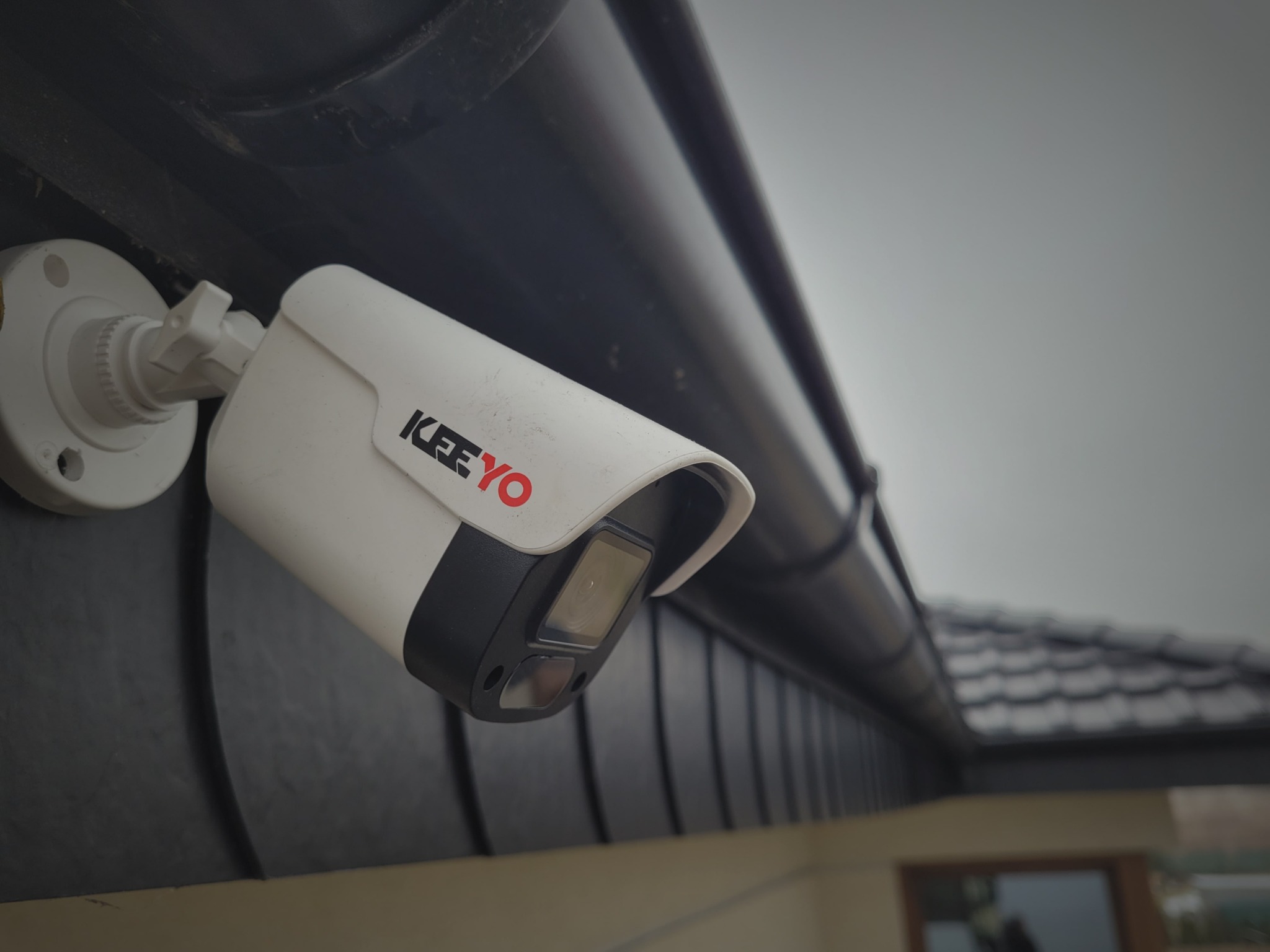 Zamontowana kamera monitoringu marki KEEYO na elewacji budynku, widoczna z bliska pod kątem. Kamera w kolorze białym z czarnymi elementami.