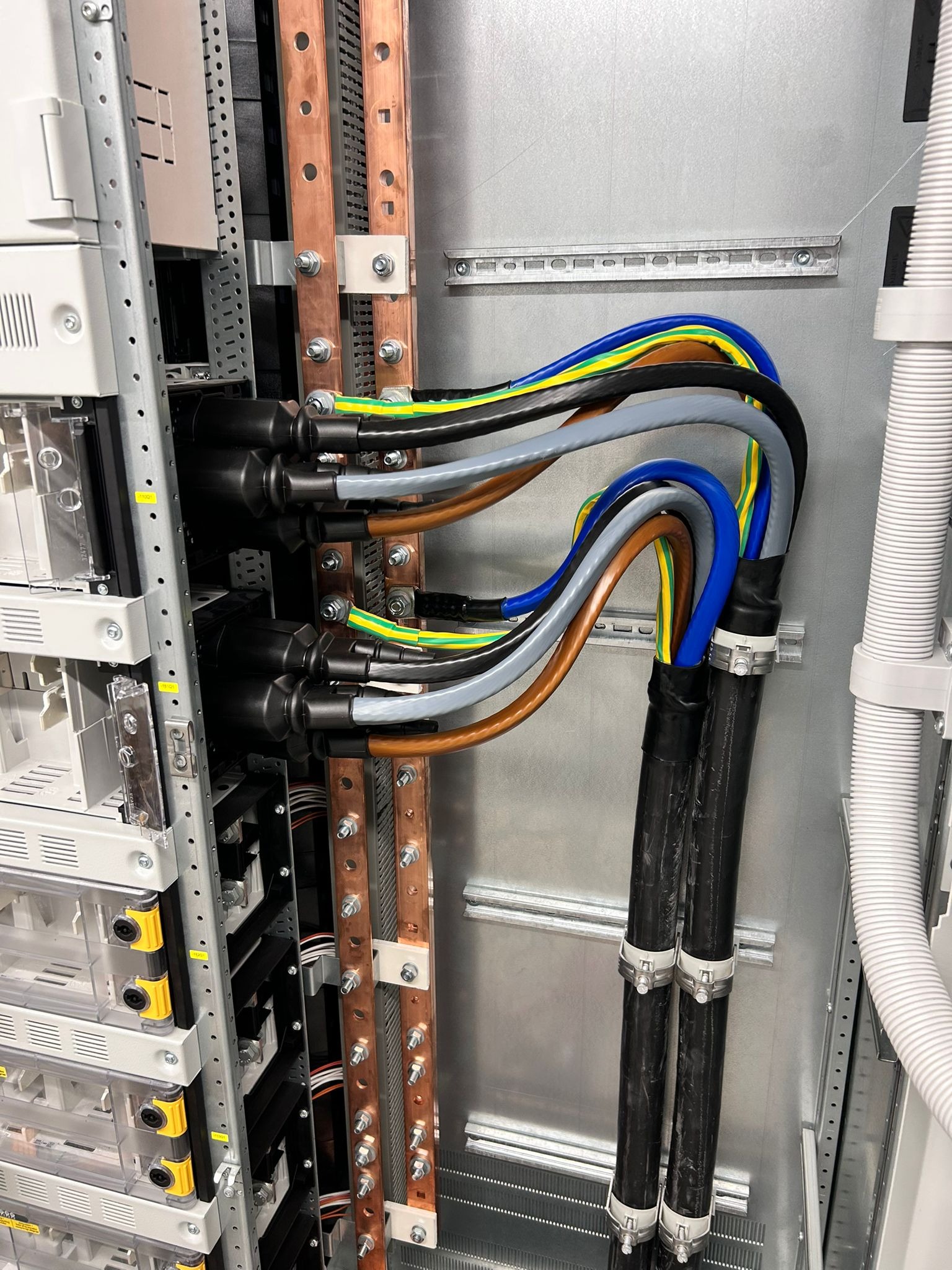 Szczegółowe ujęcie szafy elektrycznej z widocznymi, profesjonalnie ułożonymi kablami w kolorowych izolacjach, prowadzącymi do listew zaciskowych z miedzianymi szynami.