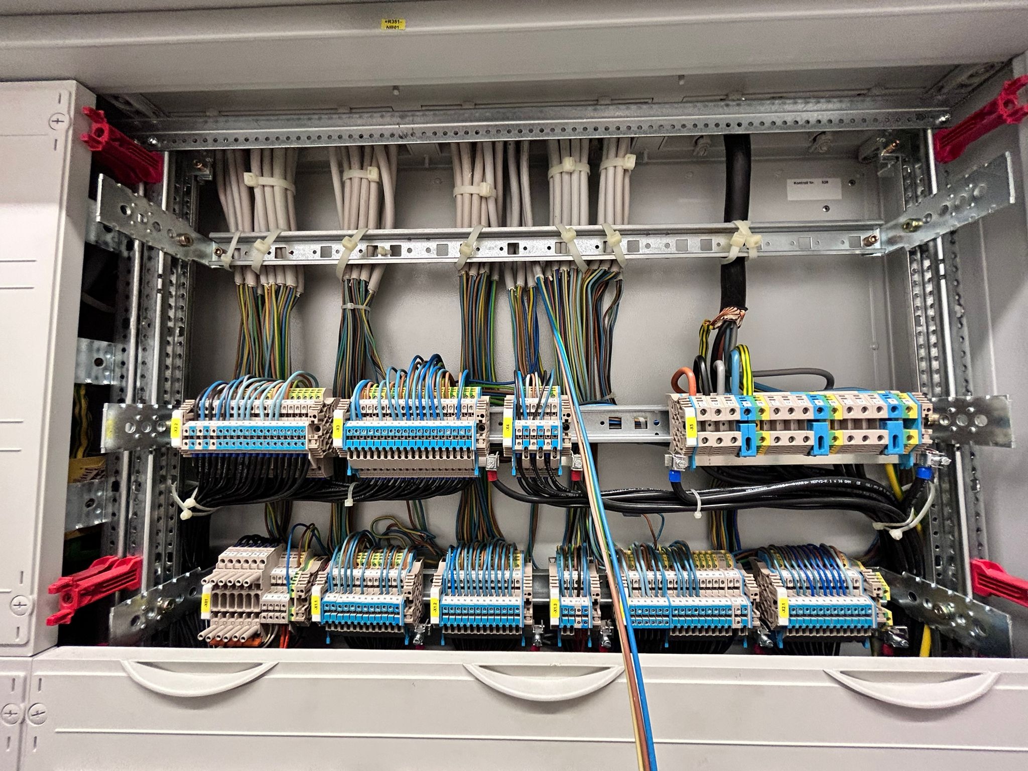 Rozdzielnia elektryczna z precyzyjnie podłączonymi przewodami o różnych kolorach, umieszczonymi w listwach. Widoczne złącza i metalowe szyny montażowe.