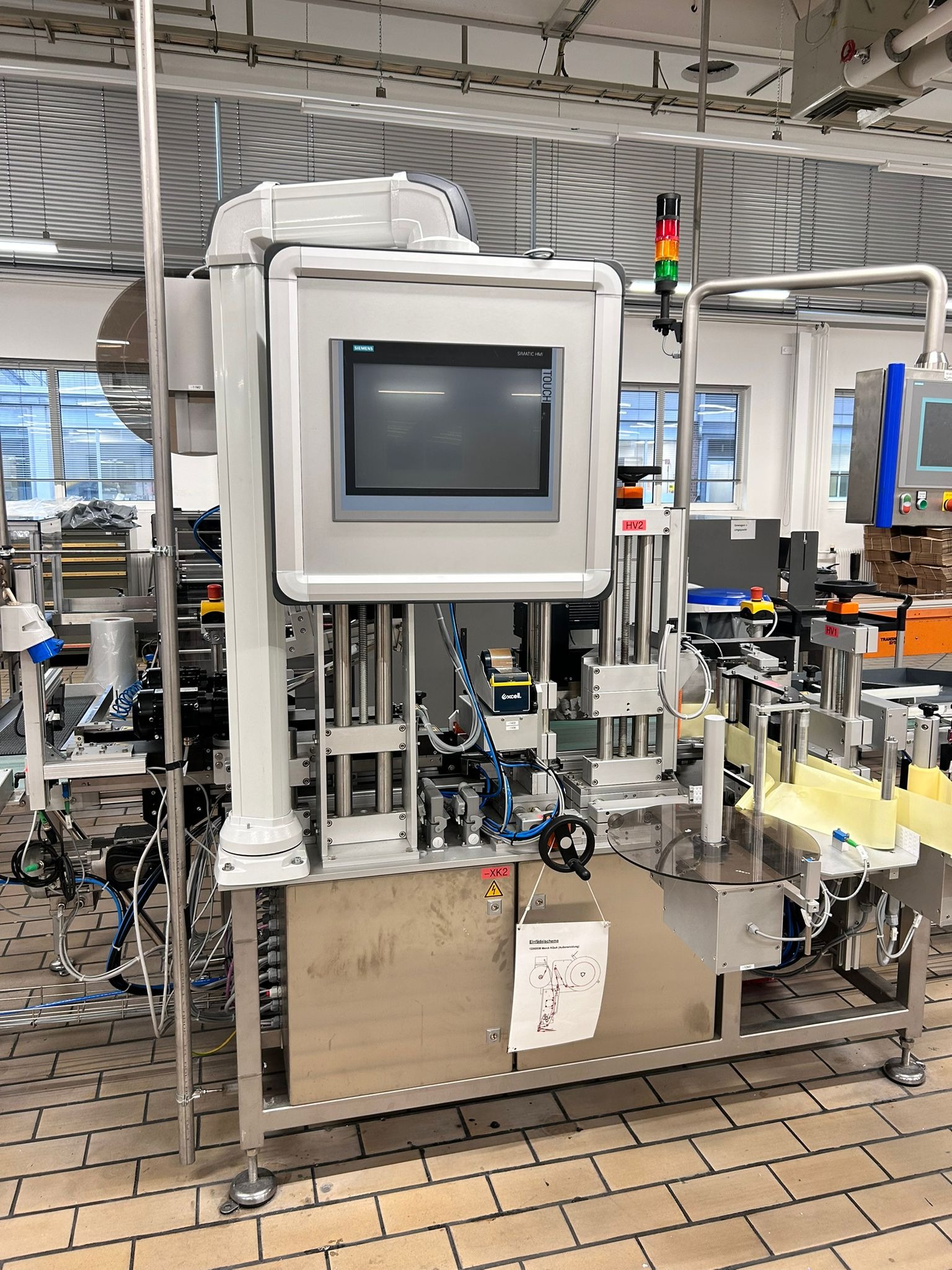 Zaawansowana maszyna przemysłowa z panelem dotykowym Siemens, widoczne przewody, czujniki i elementy mechaniczne, ustawiona na podłodze z cegieł w hali produkcyjnej.