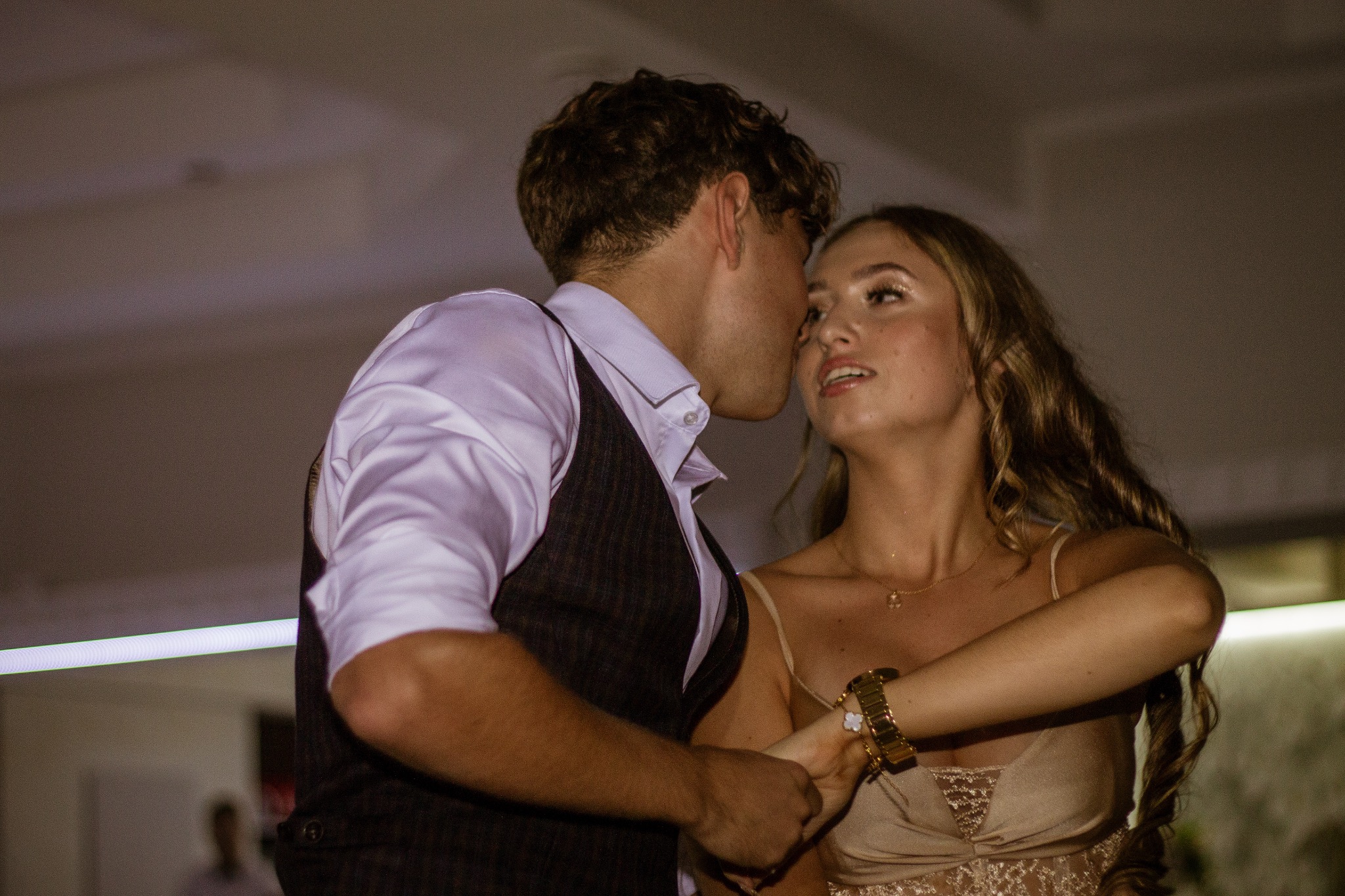 Para w tańcu: mężczyzna w kamizelce obejmuje kobietę w sukience, ona patrzy w górę. Scena z imprezy, ciepłe oświetlenie, widoczny fragment parkietu.