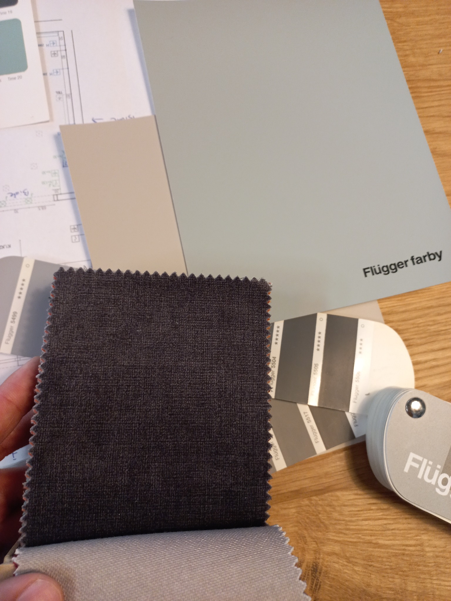 Próbki materiałów i paleta kolorów Flügger farby na drewnianym blacie. Widoczny plan mieszkania. Wybór kolorystyki i tkanin do aranżacji wnętrza.