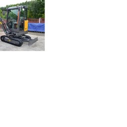 DJ MARIO-WODAN SP. Z O.O. - Szara minikoparka Volvo z łyżką i lemieszem na żwirowym podłożu, z widocznym logo Volvo na ramieniu. Tło stanowi budynek i zieleń.