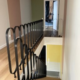 Art-Spaw Goleniów - Nowoczesna balustrada schodowa z czarnego metalu, z charakterystycznymi zaokrąglonymi elementami, na drewnianych schodach w jasnym wnętrzu.