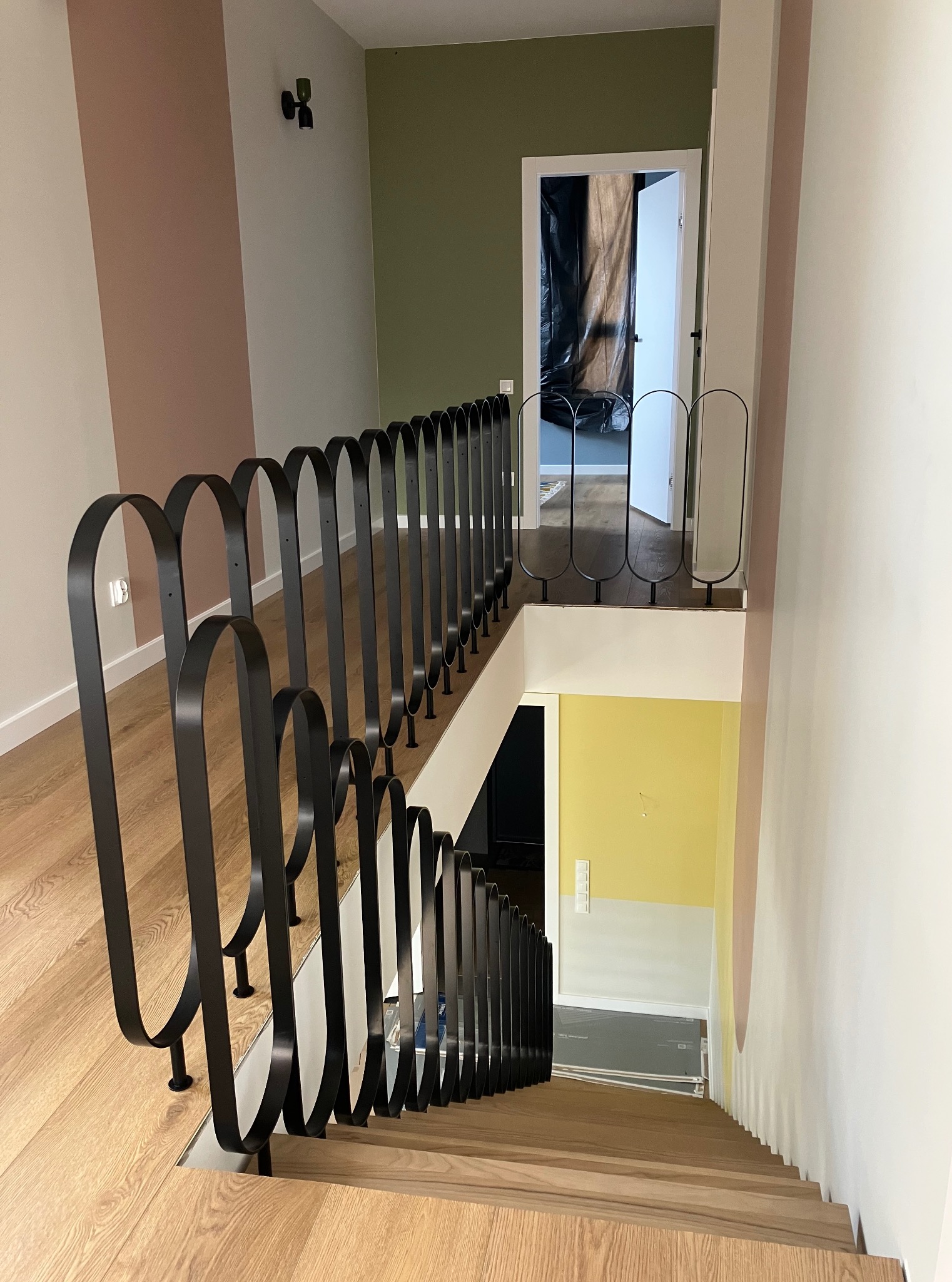 Nowoczesna balustrada schodowa z czarnego metalu, z charakterystycznymi zaokrąglonymi elementami, na drewnianych schodach w jasnym wnętrzu.