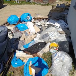 Jakub z Człuchowa - Sterta gruzu i odpadów budowlanych w workach, z fragmentem ceglanego budynku w tle. Widoczne palety i resztki materiałów budowlanych.