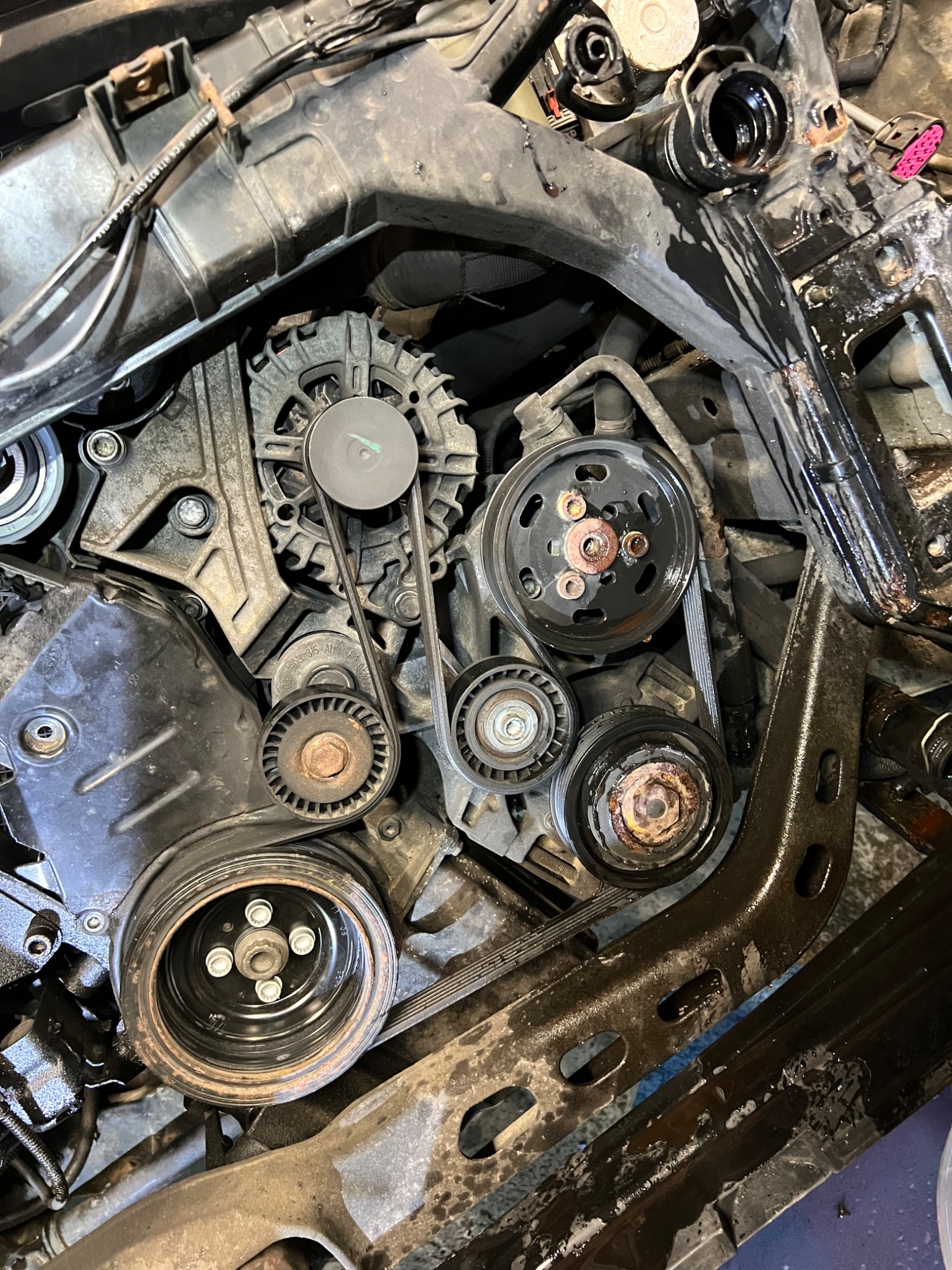 Detaliczny widok wnętrza silnika samochodowego z paskiem klinowym, kołami pasowymi i elementami metalowymi, ukazujący złożoność i stan techniczny.