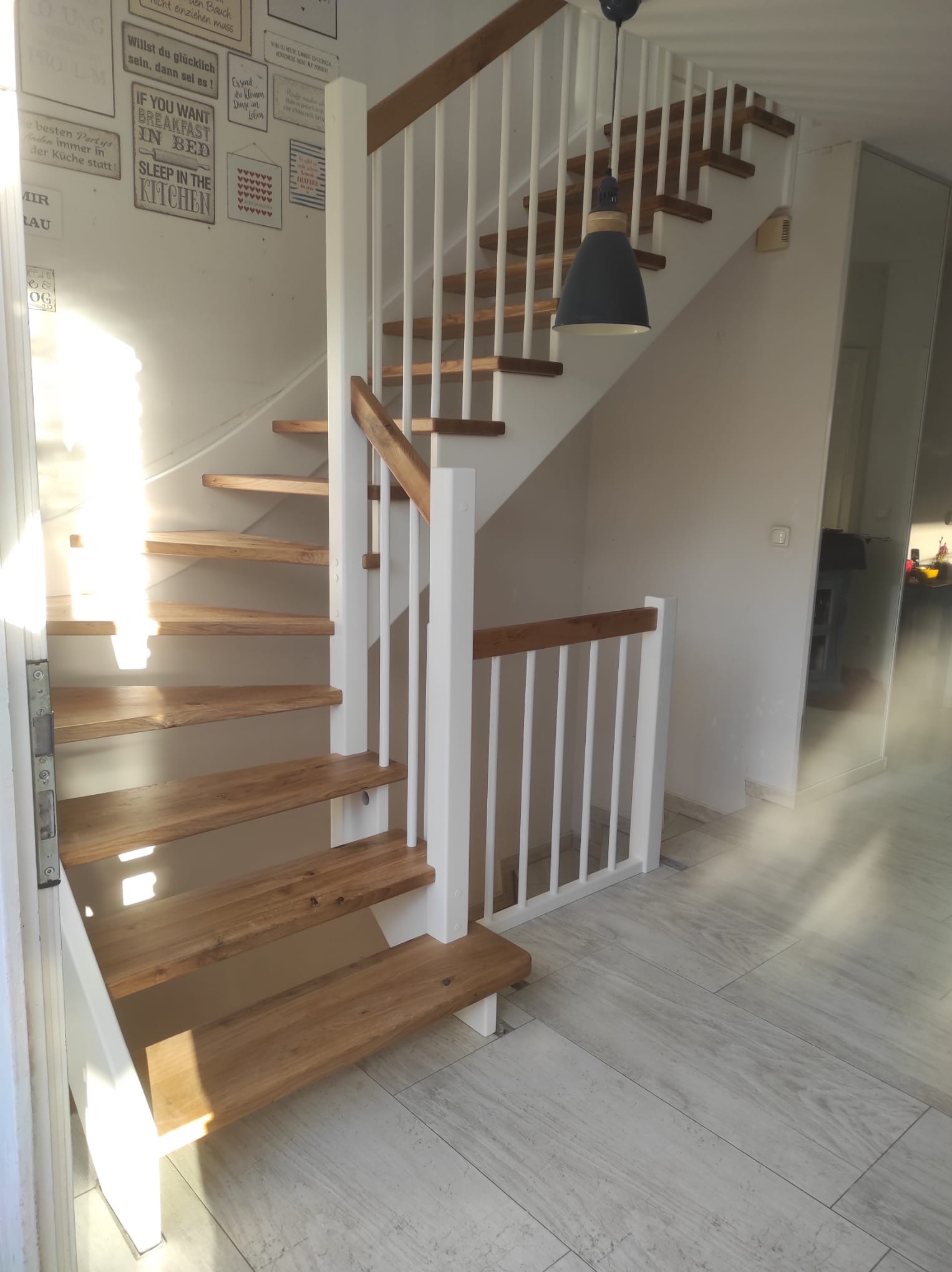 Jasne drewniane schody z białymi barierkami w nowoczesnym wnętrzu. Oświetlenie punktowe podkreśla naturalny odcień drewna i subtelny wzór na ścianie.