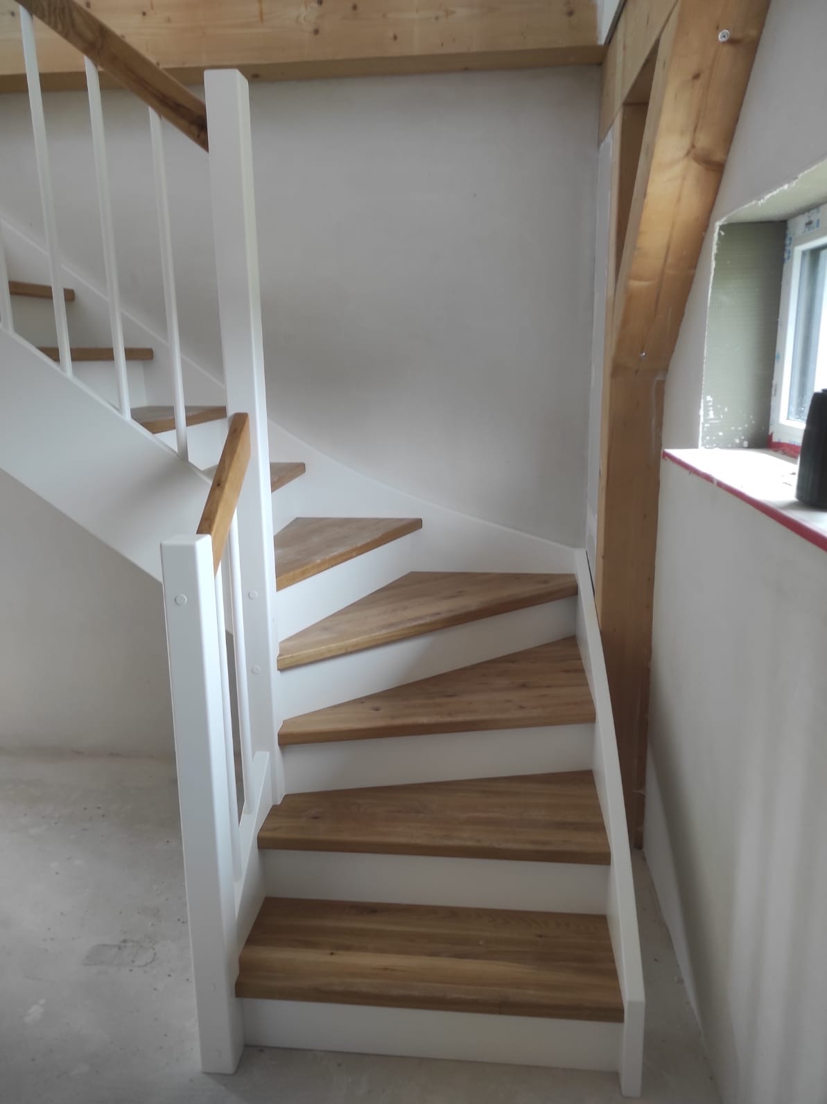 Drewniane schody z białymi barierkami w Bogusławiu. Jasne drewno stopni kontrastuje z bielą elementów konstrukcyjnych. Widoczny fragment okna i drewniany element stropu.
