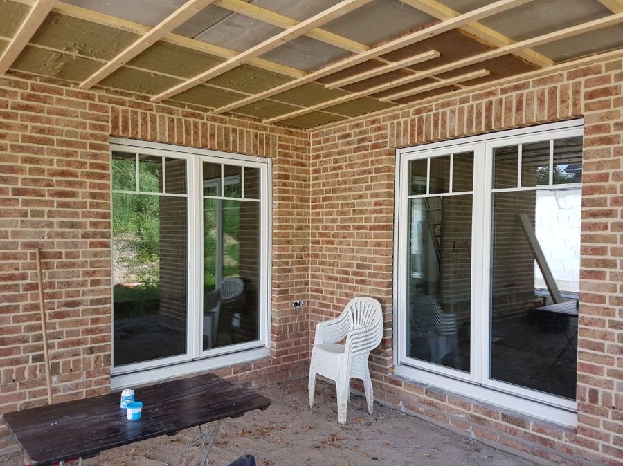 Montaż okien PCV w nowym budynku z cegły. Widoczne ocieplenie sufitu i białe ramy okienne.