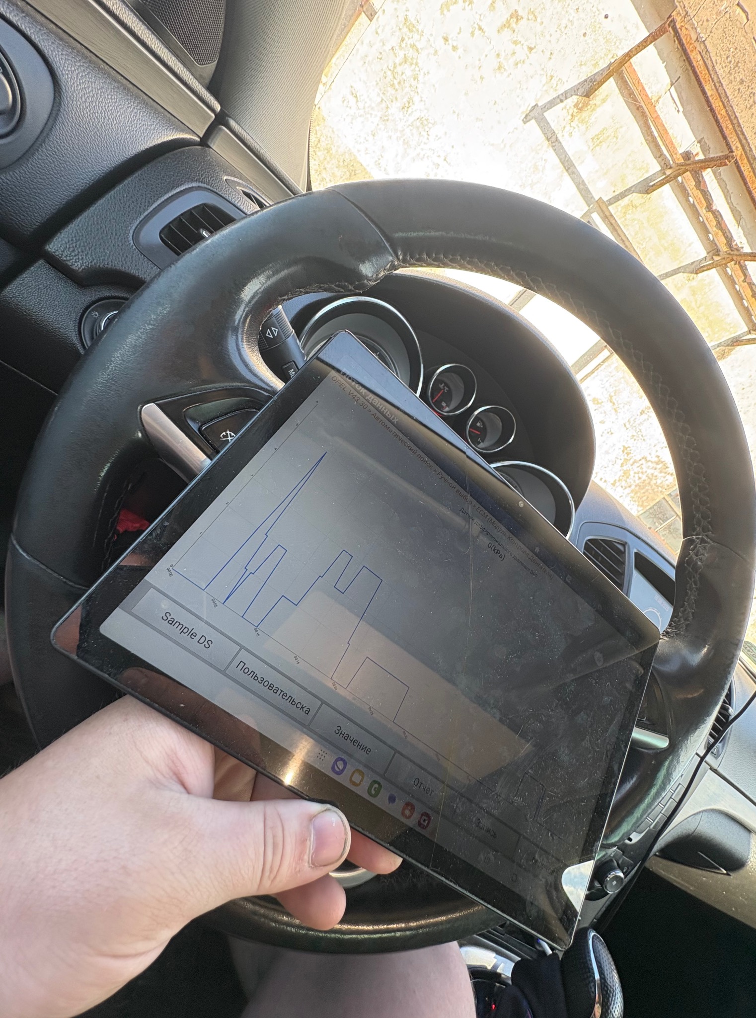 Diagnostyka pojazdu: tablet z wykresem parametrów pracy silnika na tle kierownicy i deski rozdzielczej samochodu Opel. Widok z wnętrza auta.