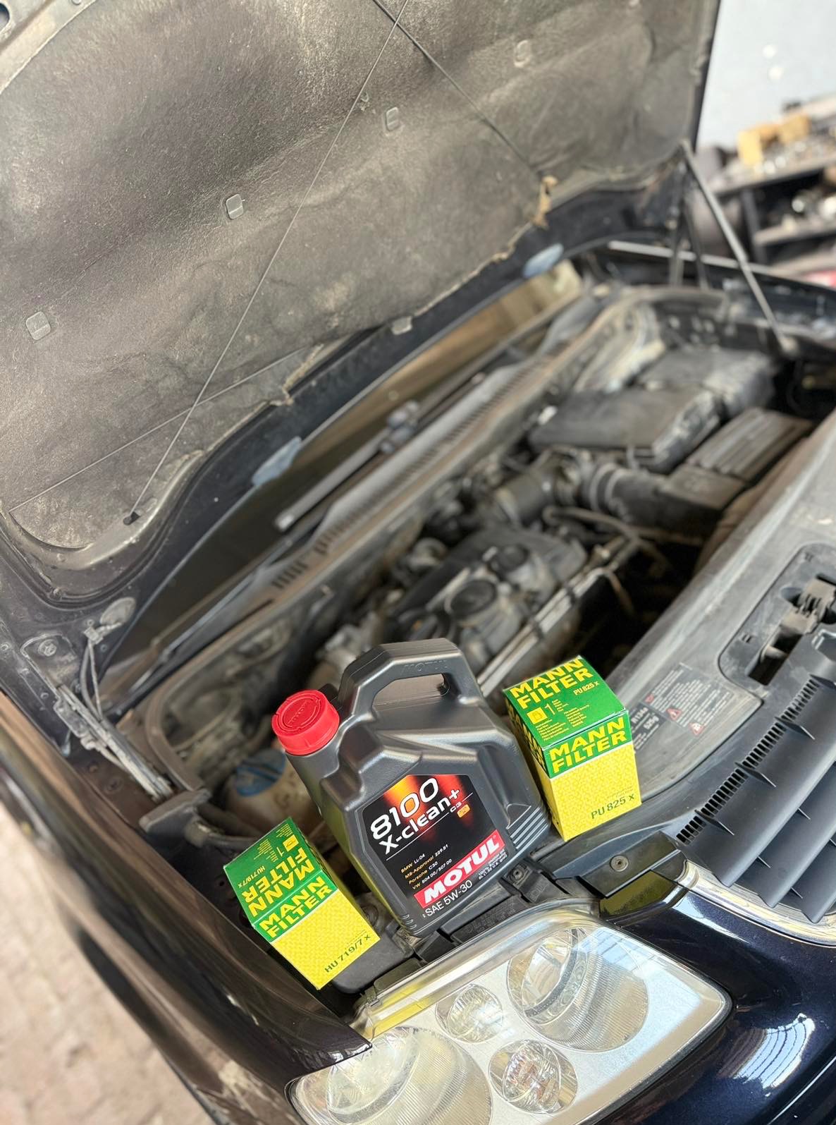 Otwarta maska samochodu z widocznym silnikiem, olejem Motul i filtrami Mann. Przygotowanie do wymiany oleju i filtrów w warsztacie.