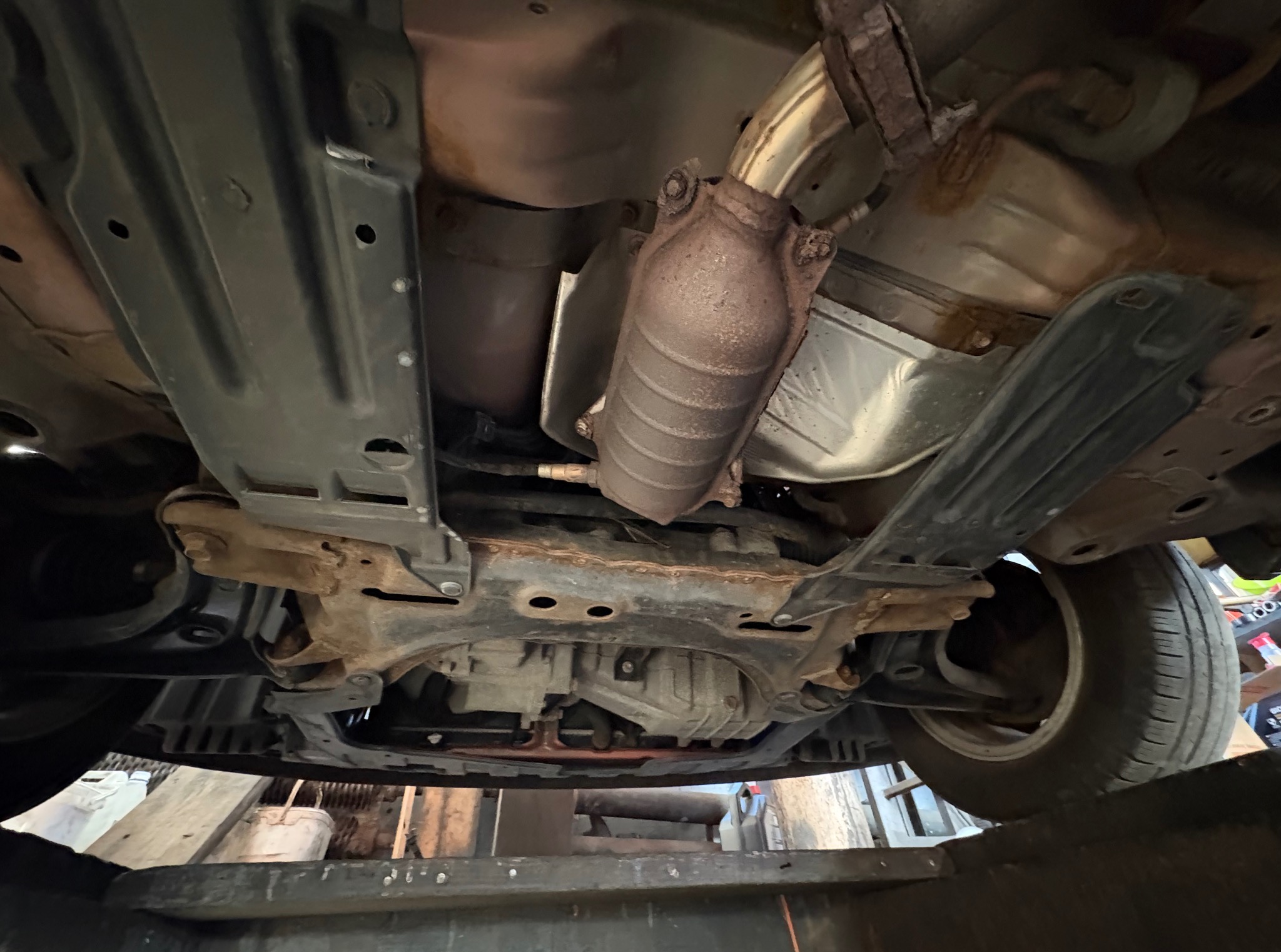 Widok podwozia samochodu z widocznym układem wydechowym, katalizatorem i elementami zawieszenia. Widoczne ślady korozji. Auto na podnośniku.