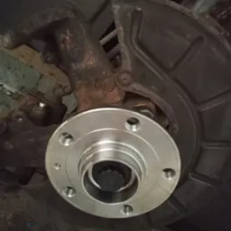 Piasta koła po wymianie, widoczne ślady korozji na elementach zawieszenia. Element układu hamulcowego w tle.