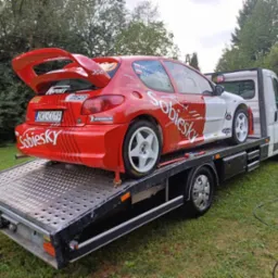 Czerwono-biały Peugeot 206 rajdowy z dużym spojlerem na lawecie. Widoczne detale: logo Sobiesky, numer 206, tablica DKL CU19, zieleń w tle.