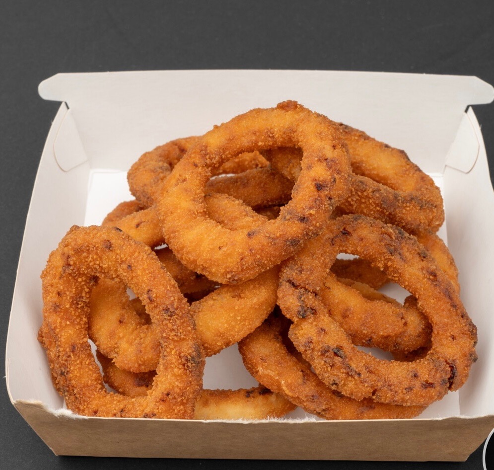 Złociste krążki cebulowe w papierowym pudełku na wynos, widoczne z bliska, na ciemnym tle. Chrupiąca panierka, ciepłe światło.