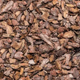 Kora sosnowa w ogrodzie, równomiernie rozłożona, tworząca naturalną, brązową powierzchnię. Widoczne fragmenty kory o różnej wielkości i odcieniach brązu.