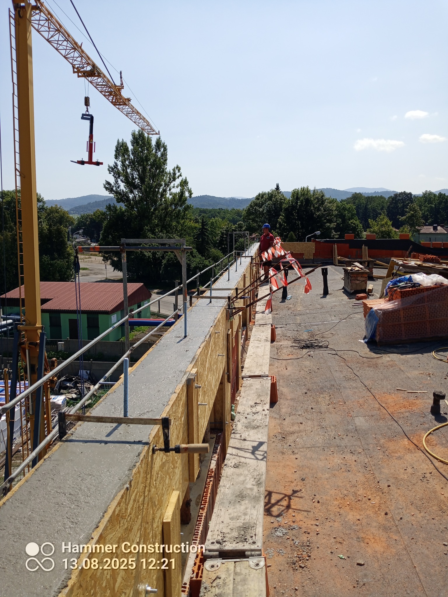 Wysoka perspektywa na formowanie betonowego elementu konstrukcyjnego na budowie, z żurawiem w tle i pracownikiem w kasku przy barierce.