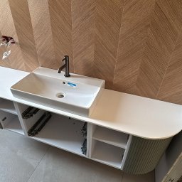 InHome AM - Nowoczesna łazienka z umywalką nablatową i szafką w kolorze zieleni. Na ścianie dekoracyjne płytki w jodełkę. Widoczne niedokończone podłączenie elektryczne.