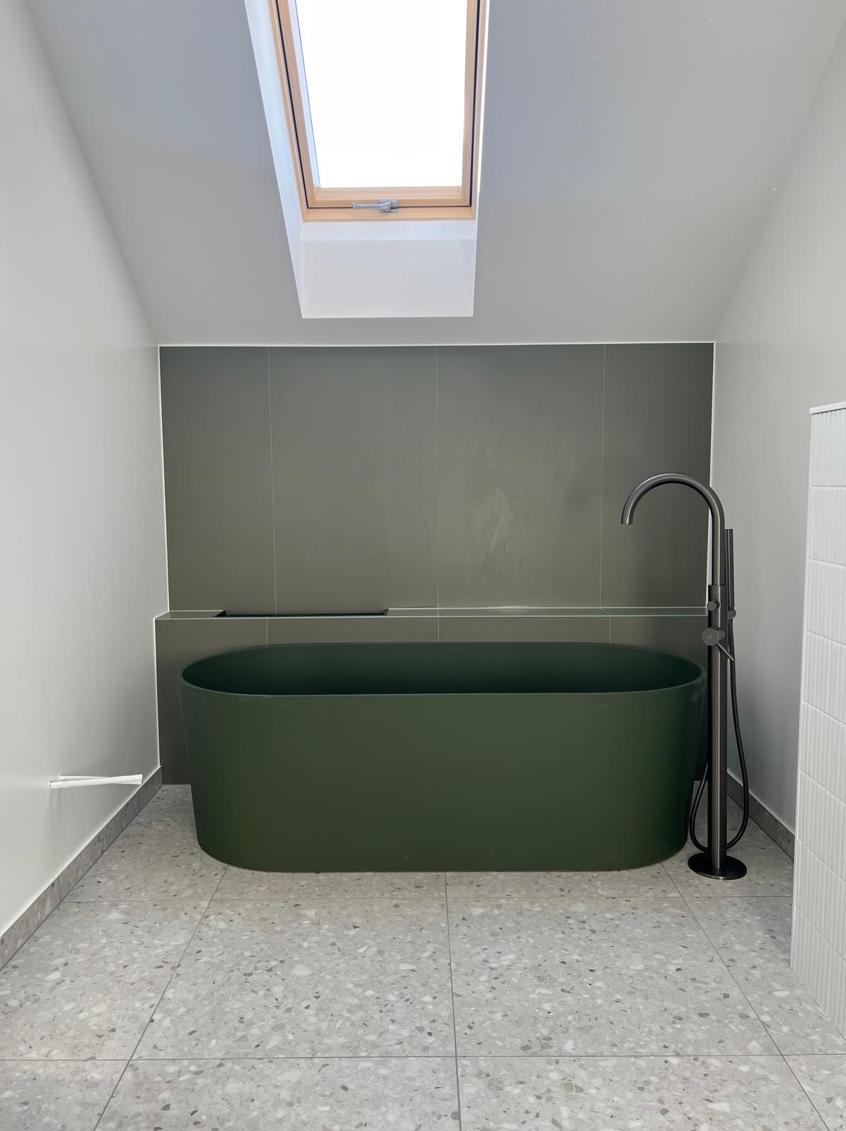 Nowoczesna łazienka na poddaszu z oliwkową wanną, szarą armaturą i płytkami lastryko. Okno dachowe doświetla wnętrze.