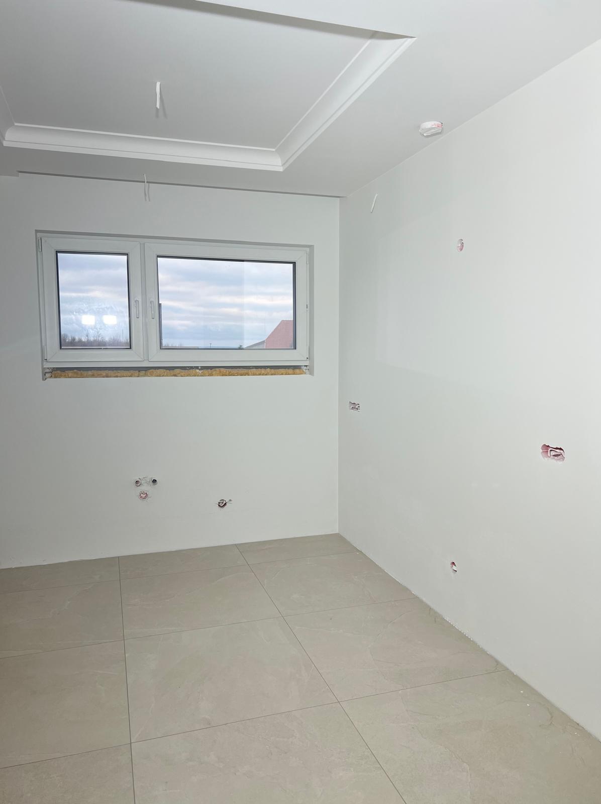 Wnętrze po remoncie: gładkie, białe ściany, jasne płytki podłogowe, okno z widokiem na zewnątrz. Widoczne punkty instalacji elektrycznej i wodnej.