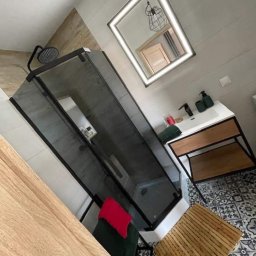 Bartosz Górski - Nowoczesna łazienka z kabiną prysznicową typu walk-in, umywalką na drewnianym stelażu i podświetlanym lustrem. Czarno-biała mozaika na podłodze.