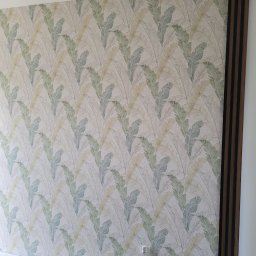 Bartosz Górski - Ściana po tapetowaniu w Starym Dzierzgoniu z wzorem liści i dekoracyjnymi panelami ściennymi. Widoczny fragment odkurzacza.