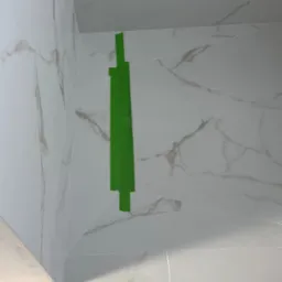 Wykończona ściana i podłoga w łazience z białych, marmurkowych płytek, zabezpieczona zieloną taśmą malarską w rogu. Widok z dołu.