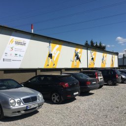 Druknij.to - Druk wielkoformatowy: Billboard reklamowy zawodów squash na ścianie budynku, zaparkowane samochody w pierwszym planie, błękitne niebo w tle.