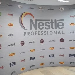 Druknij.to - Ścianka reklamowa z logo Nestle Professional i logotypami różnych marek spożywczych na szarym tle, używana podczas wydarzeń branżowych.