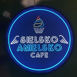 Druknij.to - Niebieski neonowy szyld kawiarni 'Sielsko Anielsko Cafe' z motywem babeczki i skrzydłami, oświetlony niebieską obwódką. Widoczne elementy montażowe.