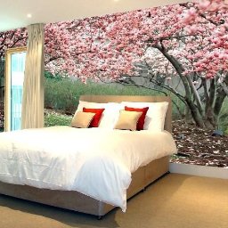 Druknij.to - Sypialnia z łóżkiem na tle fototapety z kwitnącą magnolią. Naturalne światło z okna po lewej stronie. Beżowa podłoga i rama łóżka.