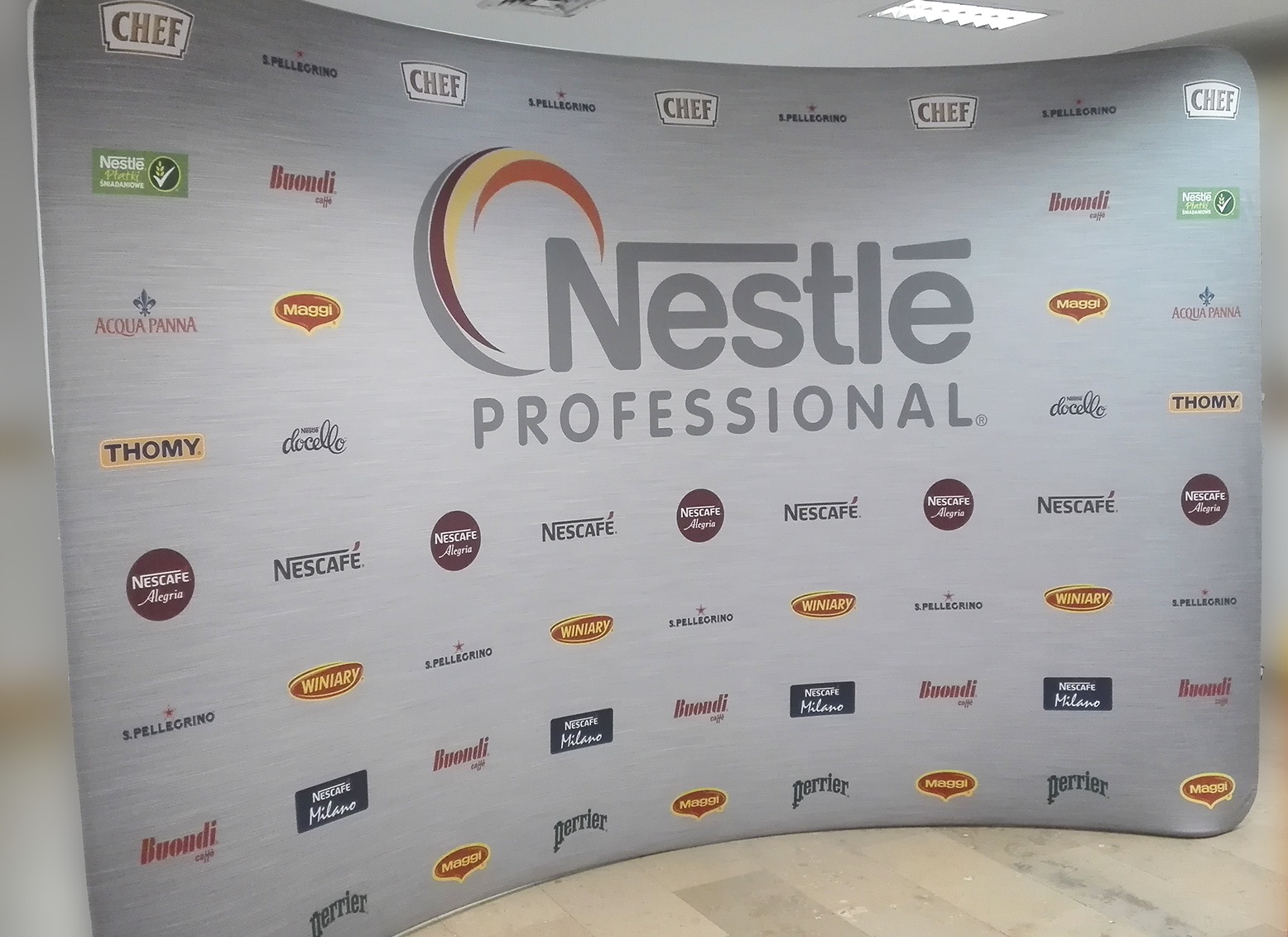 Ścianka reklamowa z logo Nestle Professional i logotypami różnych marek spożywczych na szarym tle, używana podczas wydarzeń branżowych.