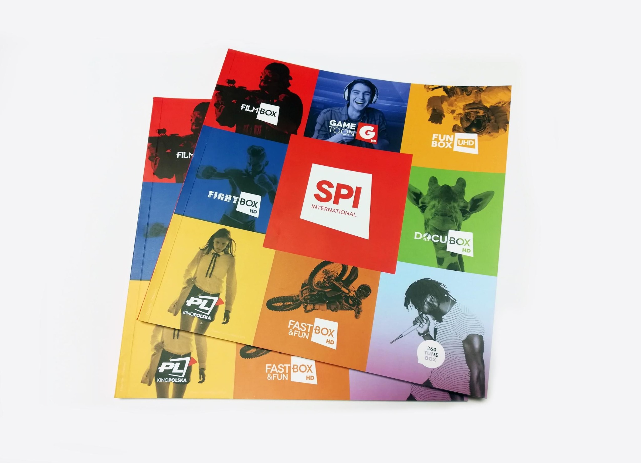Stos kolorowych broszur reklamowych SPI International, z logotypami kanałów: FilmBox, GameToon, FunBox UHD, FightBox, DocuBox, Kino Polska, FastBox&Fun, 360 Tune Box.