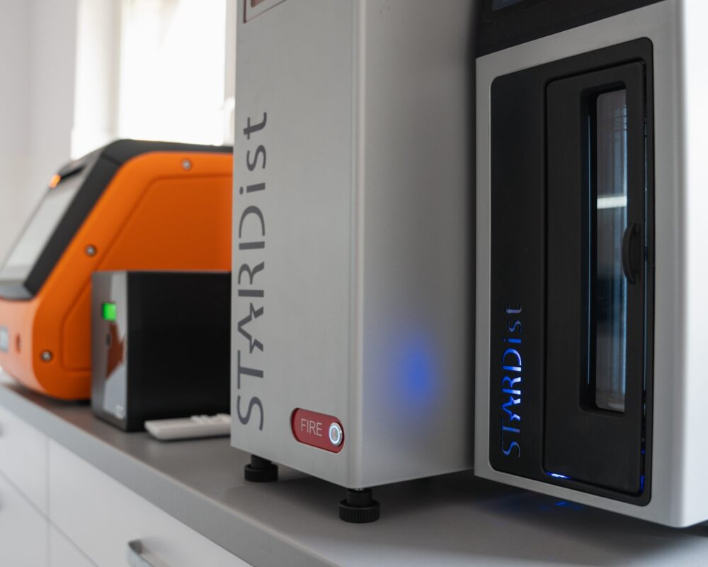 Zestaw urządzeń laboratoryjnych marki STARDist: analizator, dysk sieciowy NAS i kontroler, ustawione na blacie. Nowoczesny design, srebrna obudowa, podświetlane elementy.