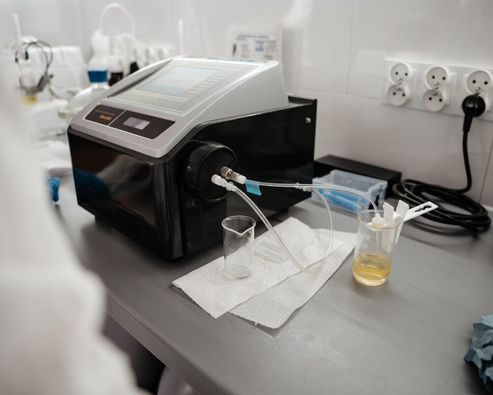 Analizator DA 640 z próbkami w zlewkach na metalowym stole laboratoryjnym. Przezroczyste wężyki i białe płytki w tle. Pomiar jakości oleju.