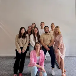 Zespół młodych, uśmiechniętych pracowników w swobodnych strojach pozuje w jasnym biurze, tworząc przyjazną atmosferę firmy. Różnorodność i pozytywna energia.