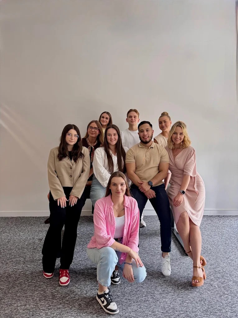 Zespół młodych, uśmiechniętych pracowników w swobodnych strojach pozuje w jasnym biurze, tworząc przyjazną atmosferę firmy. Różnorodność i pozytywna energia.