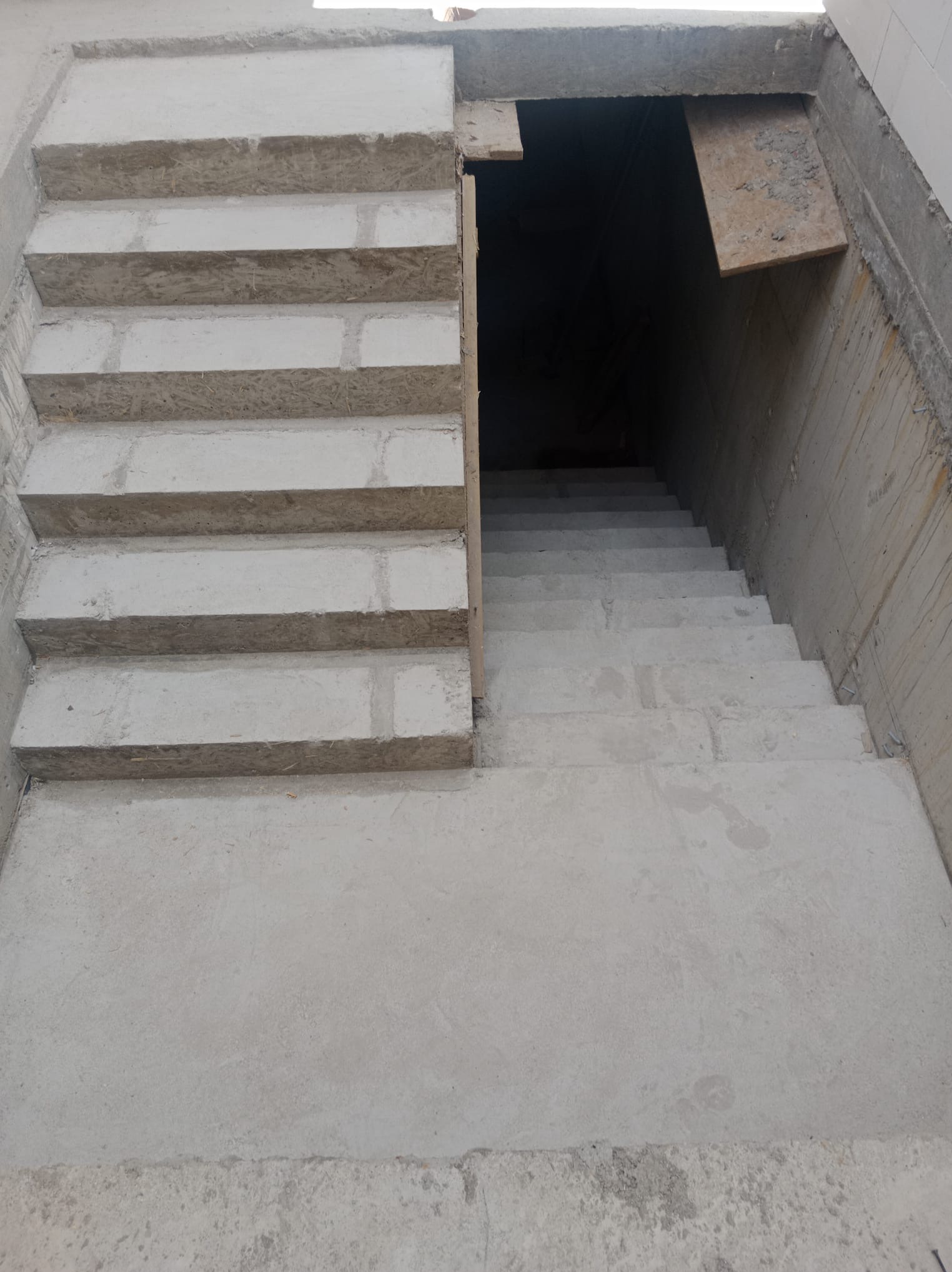 Betonowe schody prowadzące w dół, widoczne ślady szalunku, surowy stan wykończenia, pionowy kadr.