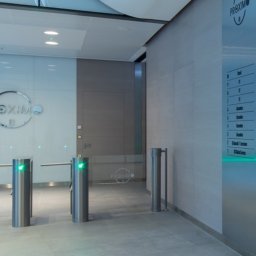 AP Budownictwo Agnieszka Lipińska - Nowoczesne wykończenie wnętrza biura w Warszawie. Szklane ściany, metalowe bramki wejściowe, minimalistyczny design. Stonowana kolorystyka i subtelne oświetlenie.