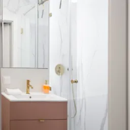 Nowoczesna łazienka z kabiną prysznicową i umywalką w kolorze pudrowego różu, złota armatura, białe marmurowe płytki. Minimalistyczny design.