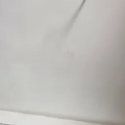 Biały kabel wystający ze ściany, świeżo po malowaniu, z widocznym cieniem na gładkiej, jednolitej powierzchni. Minimalistyczne ujęcie detalu wykończenia wnętrza.