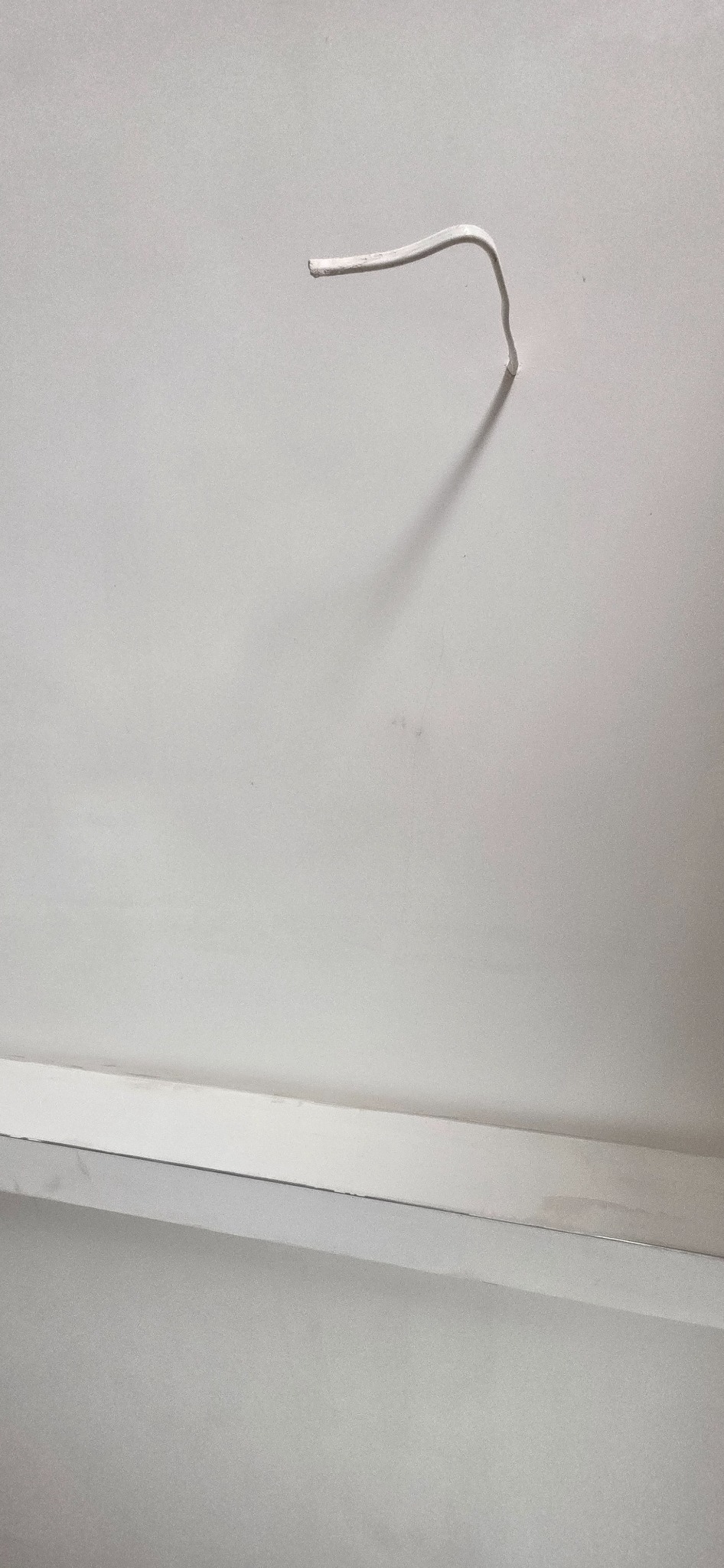 Biały kabel wystający ze ściany, świeżo po malowaniu, z widocznym cieniem na gładkiej, jednolitej powierzchni. Minimalistyczne ujęcie detalu wykończenia wnętrza.